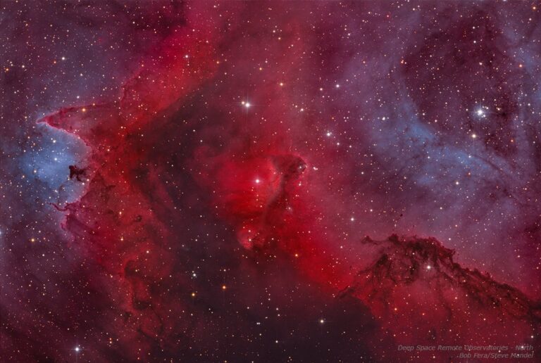 Image of the Soul Nebula, a vast red emission nebula in the constellation Cassiopeia. Bright tendrils of glowing hydrogen gas weave around dark dust lanes, with embedded star clusters illuminating the cloud from within.